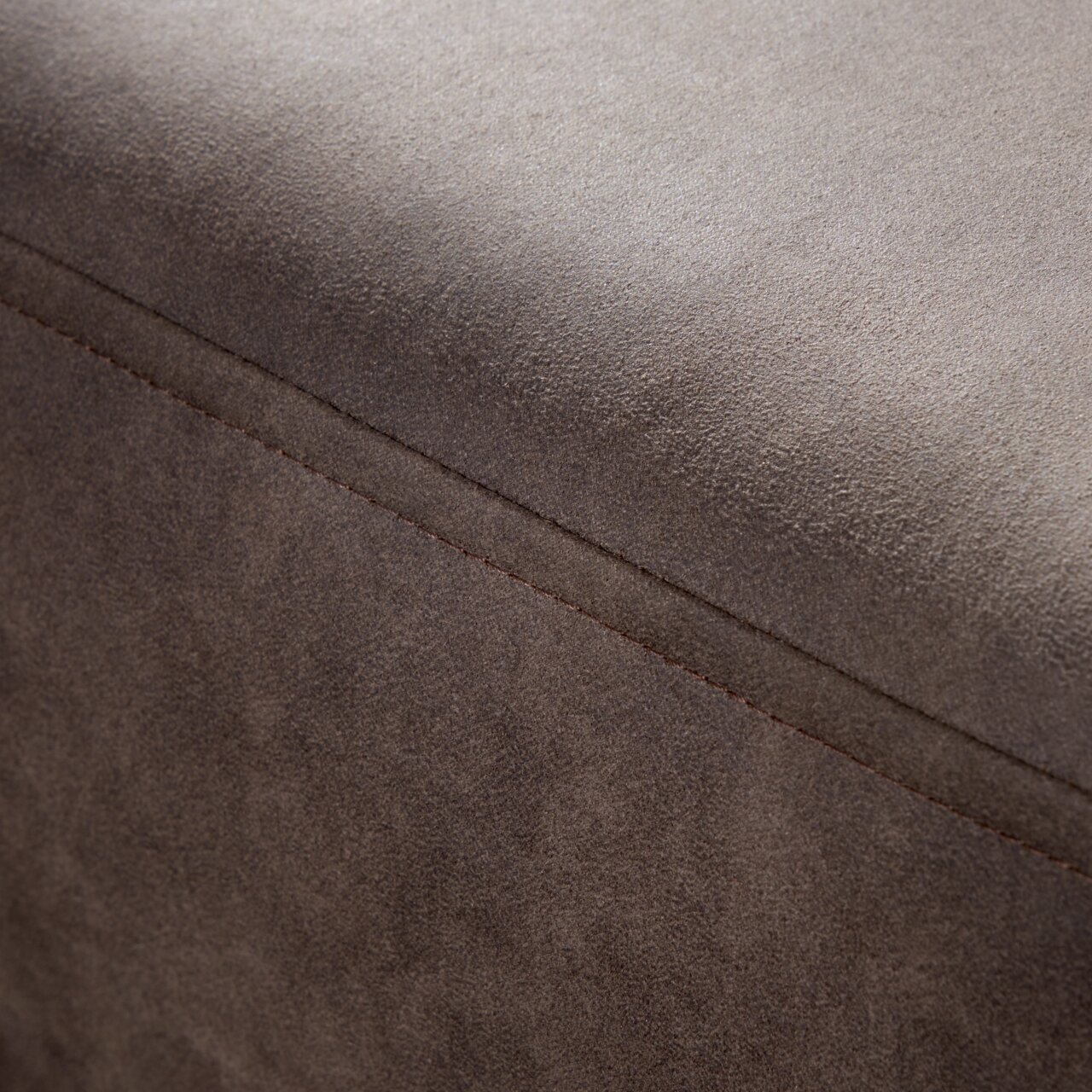 Nahaufnahme einer braunen, texturierten Oberfläche eines Möbelstücks, möglicherweise ein Hocker oder eine Rundecke, mit sichtbarer Naht. Perspektive von oben.