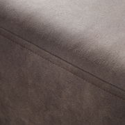 Nahaufnahme einer braunen, texturierten Oberfläche eines Möbelstücks, möglicherweise ein Hocker oder eine Rundecke, mit sichtbarer Naht. Perspektive von oben.