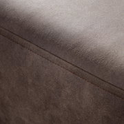 Nahaufnahme einer braunen, texturierten Oberfläche eines Möbelstücks, möglicherweise ein Hocker oder eine Rundecke, mit sichtbarer Naht. Perspektive von oben.