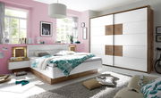 Modernes Schlafzimmer mit einem weißen Schwebetürenschrank und einer Bettanlage in Holzoptik, seitliche Perspektive