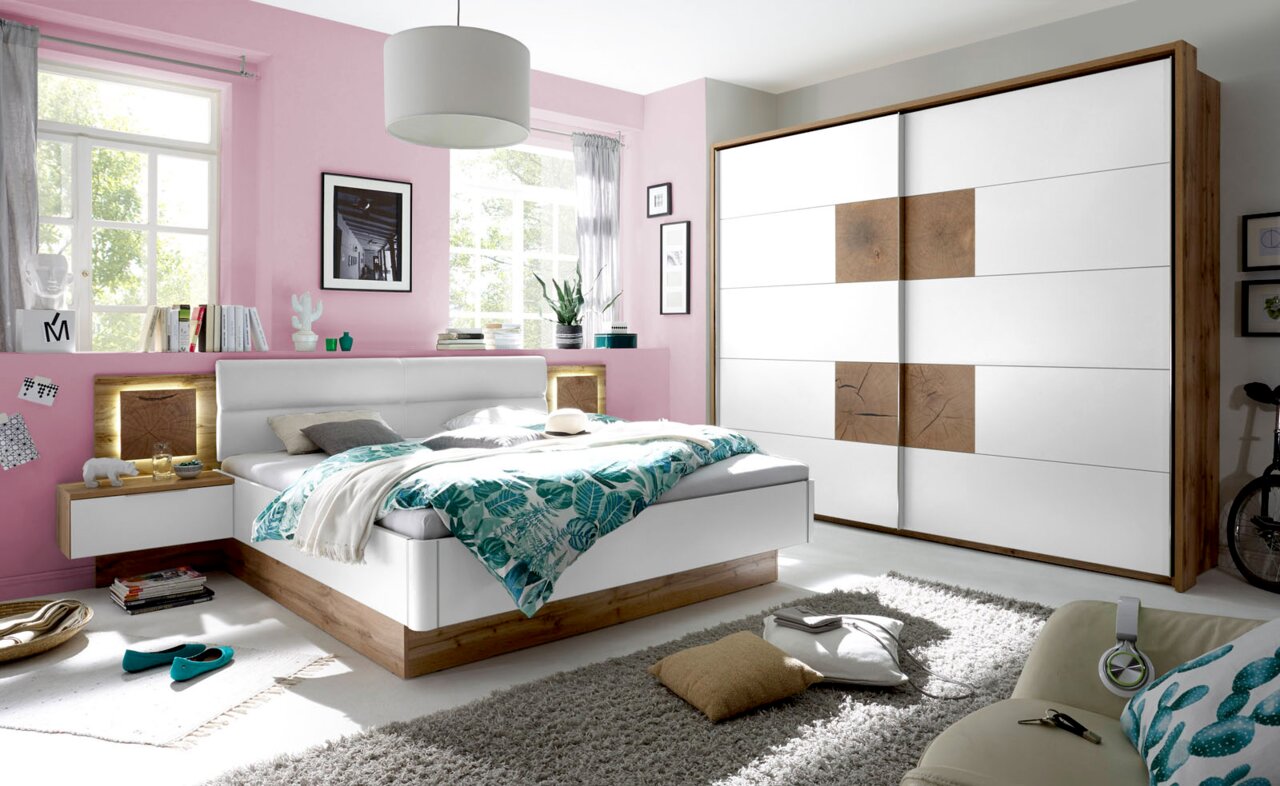 Z2 Bettanlage CAPRI Modernes Schlafzimmer mit einem weißen Schwebetürenschrank und einer Bettanlage in Holzoptik, seitliche Perspektive