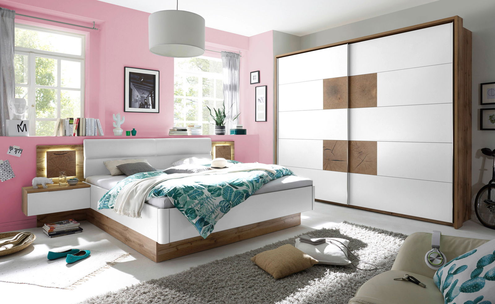 Modernes Schlafzimmer mit einem weißen Schwebetürenschrank und einer Bettanlage in Holzoptik, seitliche Perspektive
