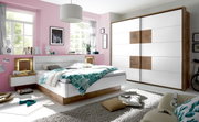 Modernes Schlafzimmer mit einem weißen Schwebetürenschrank und einer Bettanlage in Holzoptik, seitliche Perspektive