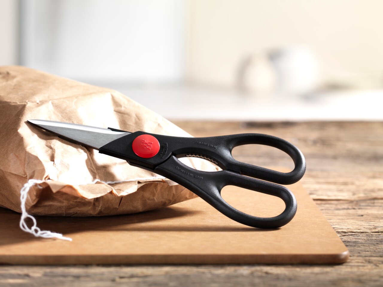 Schwarze Vielzweckschere mit rotem Detail, liegend auf einem Holzbrett, von der Seite fotografiert.