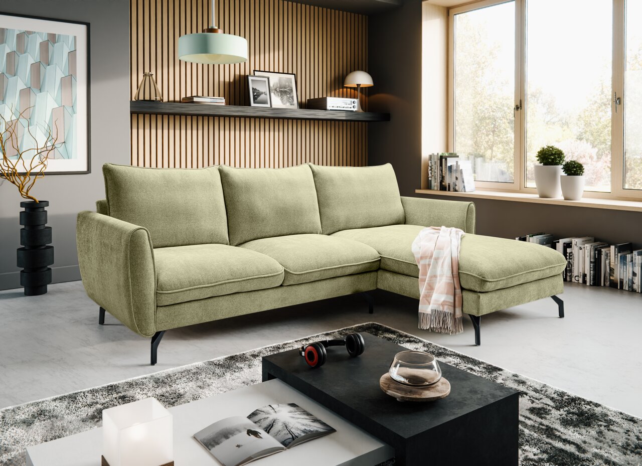 Hellgrünes L-förmiges Ecksofa mit Recamiere rechts und schwarzen Metallfüßen im modernen Wohnzimmer, fotografiert in frontaler leicht schräger Perspektive von links.