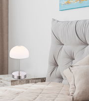 Moderne Tischleuchte SNOWFLAKE auf einem Nachttisch neben einem gepolsterten Kopfteil, seitliche Perspektive.