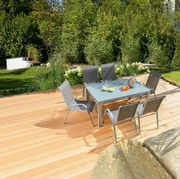 Moderner Gartentisch mit Glasplatte und sechs Stühlen auf einer Holzterrasse, umgeben von grüner Gartenlandschaft, aus der Vogelperspektive fotografiert.