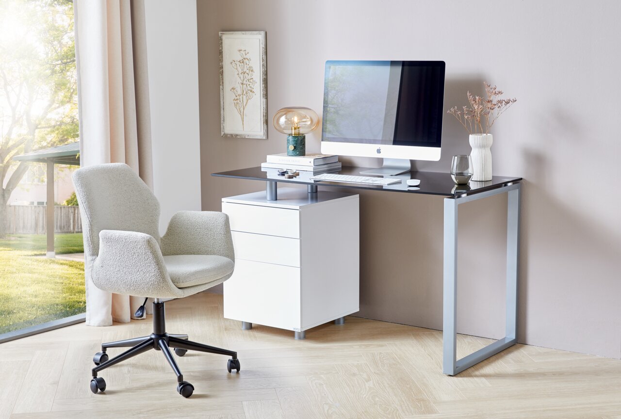 Moderner Schreibtisch mit Glasplatte und Metallrahmen, ausgestattet mit einem weißen Rollcontainer und einem Computer, seitliche Perspektive.