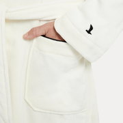 Nahaufnahme eines weißen Bademantels mit Schalkragen, einer Hand in der Tasche und einem gestickten Logo auf dem Ärmel.