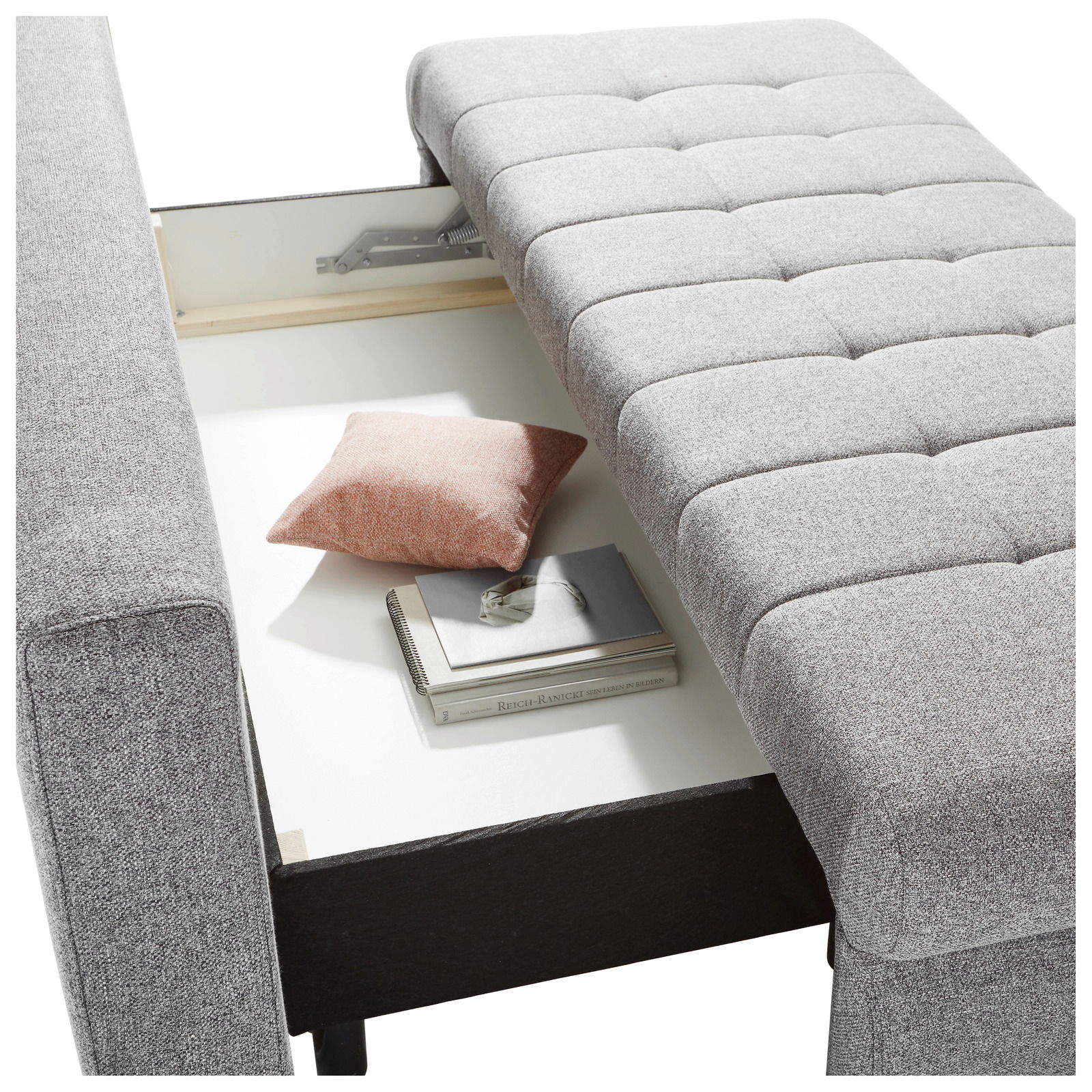 Graues Funktionssofa mit geöffneter Aufbewahrungsbox, von oben fotografiert. Ein rosa Kissen und Bücher sind im Stauraum sichtbar.