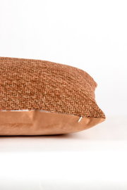 Close-up vanuit zijaanzicht van een decoratief sierkussen in warm roestbruin, met een grof geweven bovenzijde en zachte fluwelen onderzijde.