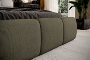 Close-up van een gestoffeerd bed met olijfgroene bekleding, gezien vanaf de zijkant