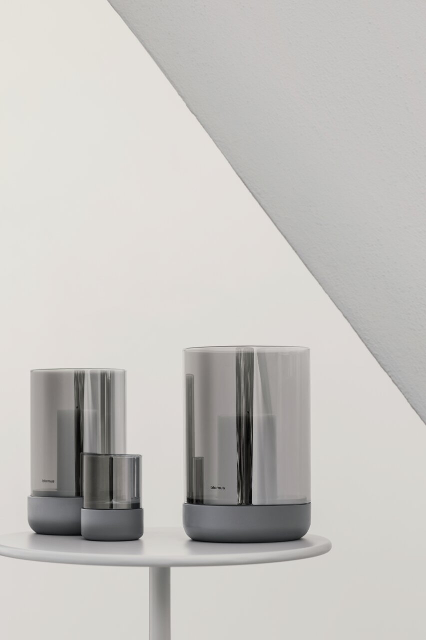 Drei Windlichter in verschiedenen Größen in Steel Gray auf einem weißen Tisch, seitliche Perspektive.