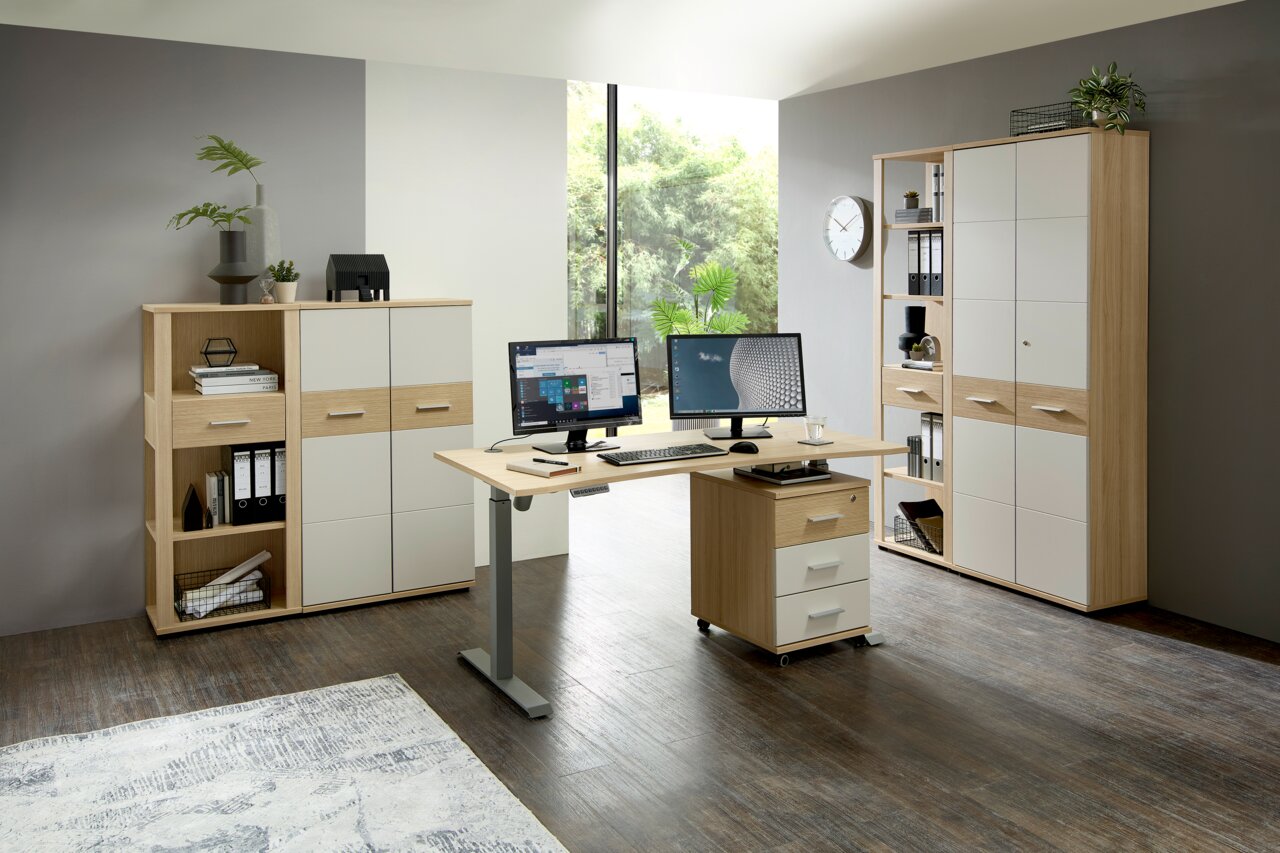 Moderner Büroraum mit einem höhenverstellbaren Schreibtisch, ausgestattet mit zwei Monitoren, Tastatur und Maus. Im Hintergrund sind Aktenschränke und Regale zu sehen. Die Perspektive zeigt den Raum von vorne.