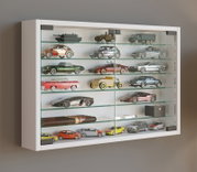 Weißer Wandvitrinenschrank mit Glasfront und mehreren Glasböden, bestückt mit Modellautos und Sammlerstücken; Ansicht schräg von vorn links