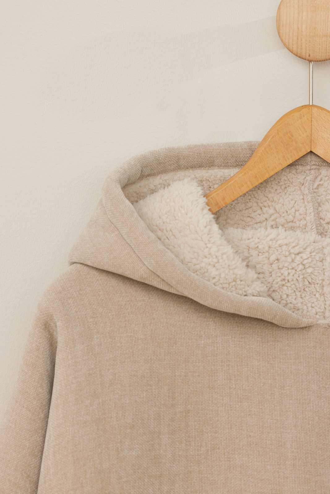 Nahaufnahme eines beigen Lounge Hoodies mit weichem Futter, auf einem Holzkleiderbügel hängend.