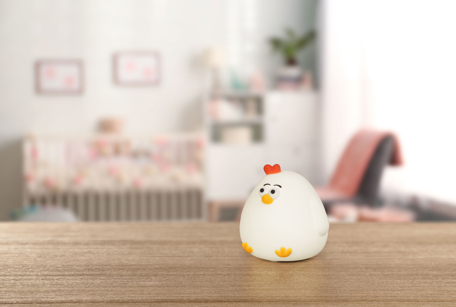 Niedliches Akku-Nachtlicht in Form eines Huhns auf einem Holztisch, im Hintergrund ein Kinderzimmer.