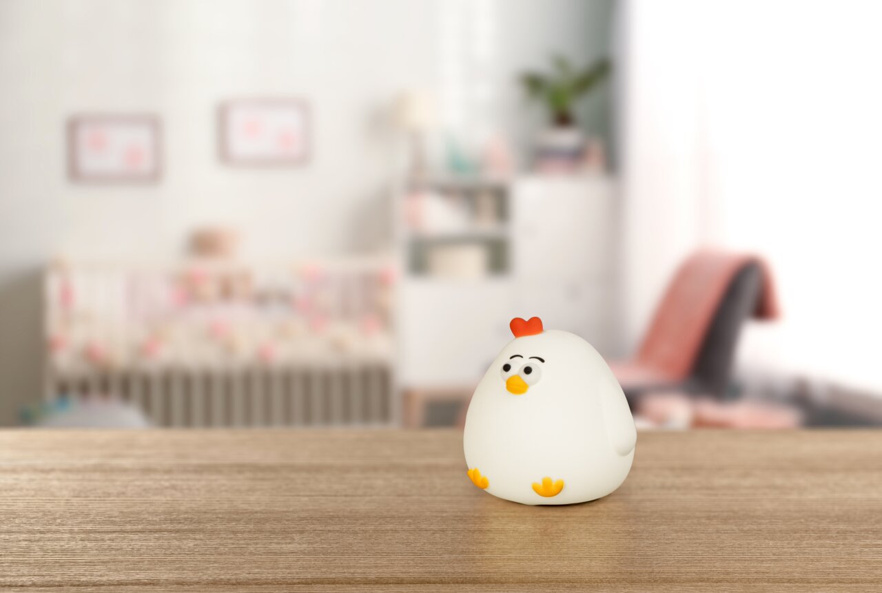 Niedliches Akku-Nachtlicht in Form eines Huhns auf einem Holztisch, im Hintergrund ein Kinderzimmer.