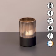 Akku-Windlicht mit geriffeltem Glaszylinder und dunklem Sockel, frontal betrachtet, mit Symbolen für USB-Ladung, Touch-Bedienung, IP54-Schutz, Fernbedienung und CCT-Farbtemperatur.