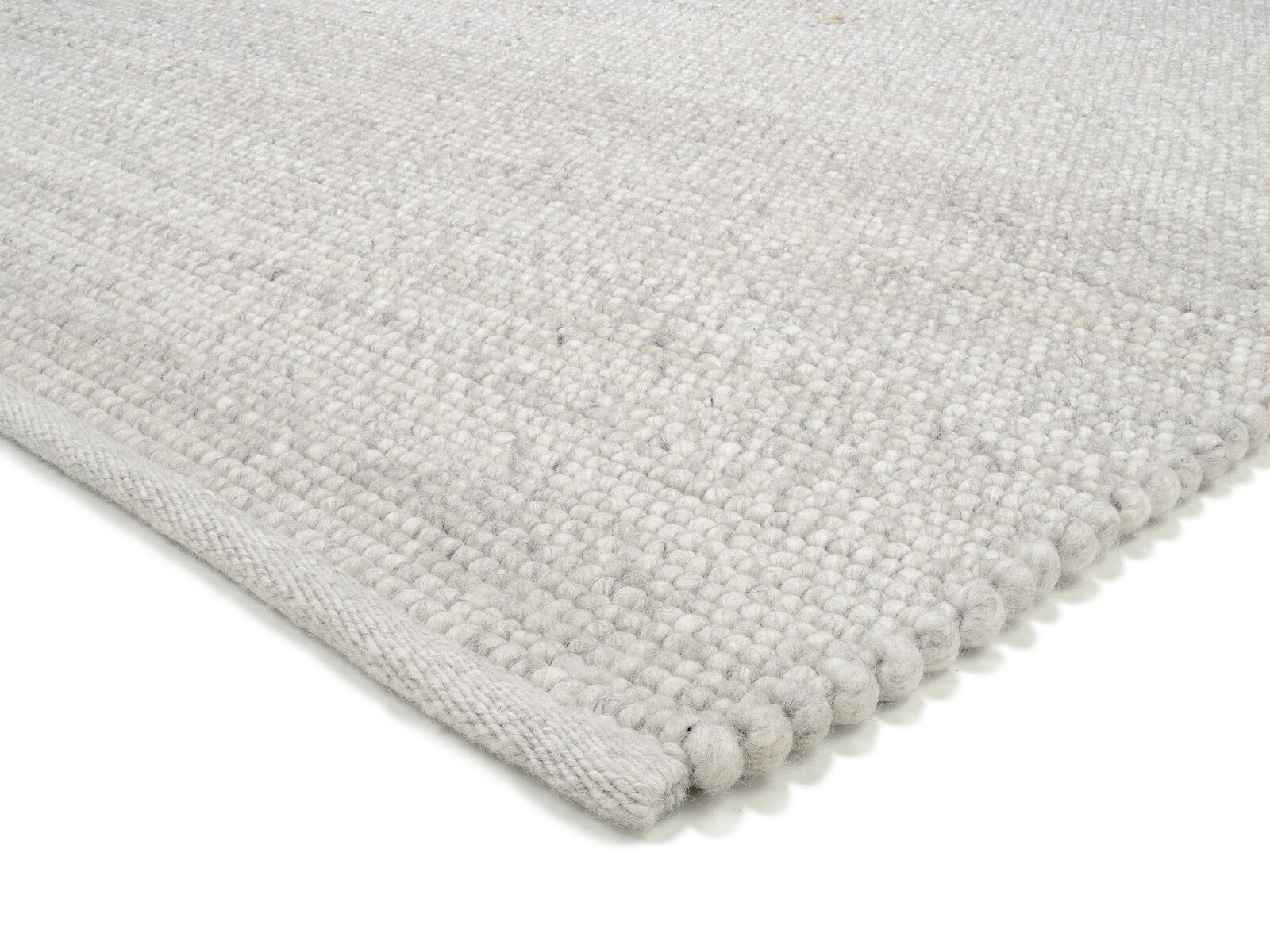 Nahaufnahme eines handgewebten Teppichs in hellem Grau, perspektivisch von der Seite aufgenommen.