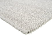 Nahaufnahme eines handgewebten Teppichs in hellem Grau, perspektivisch von der Seite aufgenommen.