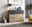 Moderne Kommode aus Holz mit drei Schubladen, obere Schublade in dunklem Grau, dekoriert mit Lampe, Büchern und Bildern, seitliche Perspektive