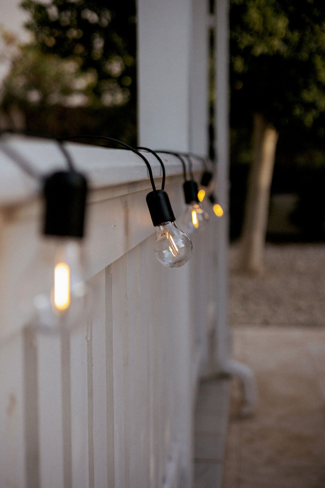 Leuchtende Outdoor-Lichterkette mit klaren Glühbirnen an einem weißen Geländer, seitliche Nahaufnahme aus schräger Perspektive entlang des Geländers