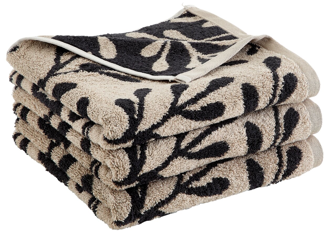 Gestapeltes Handtuch mit schwarzem Blattmuster auf beigem Hintergrund, seitliche Perspektive