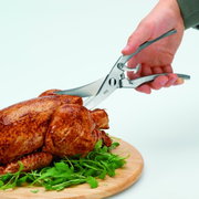 Geflügelschere mit Feder in der Hand, die ein gebratenes Hähnchen auf einem Holzbrett schneidet, seitliche Perspektive