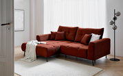 Rode hoekbank met poef aan de linkerkant, versierd met kussens en een deken, in een moderne woonkamer met een lichte houten vloer en een staande lamp, gezien vanaf links vooraan.