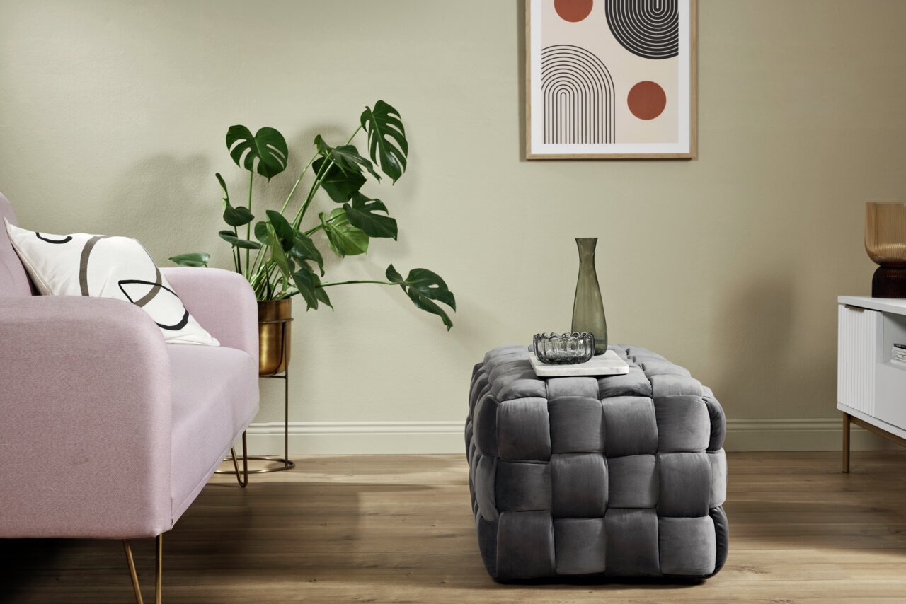 Grauer, gepolsterter Hocker in einem modernen Wohnzimmer, seitliche Perspektive