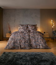 Bettwäsche-Set mit tropischem Blattmuster in einem modernen Schlafzimmer, frontal aufgenommen.