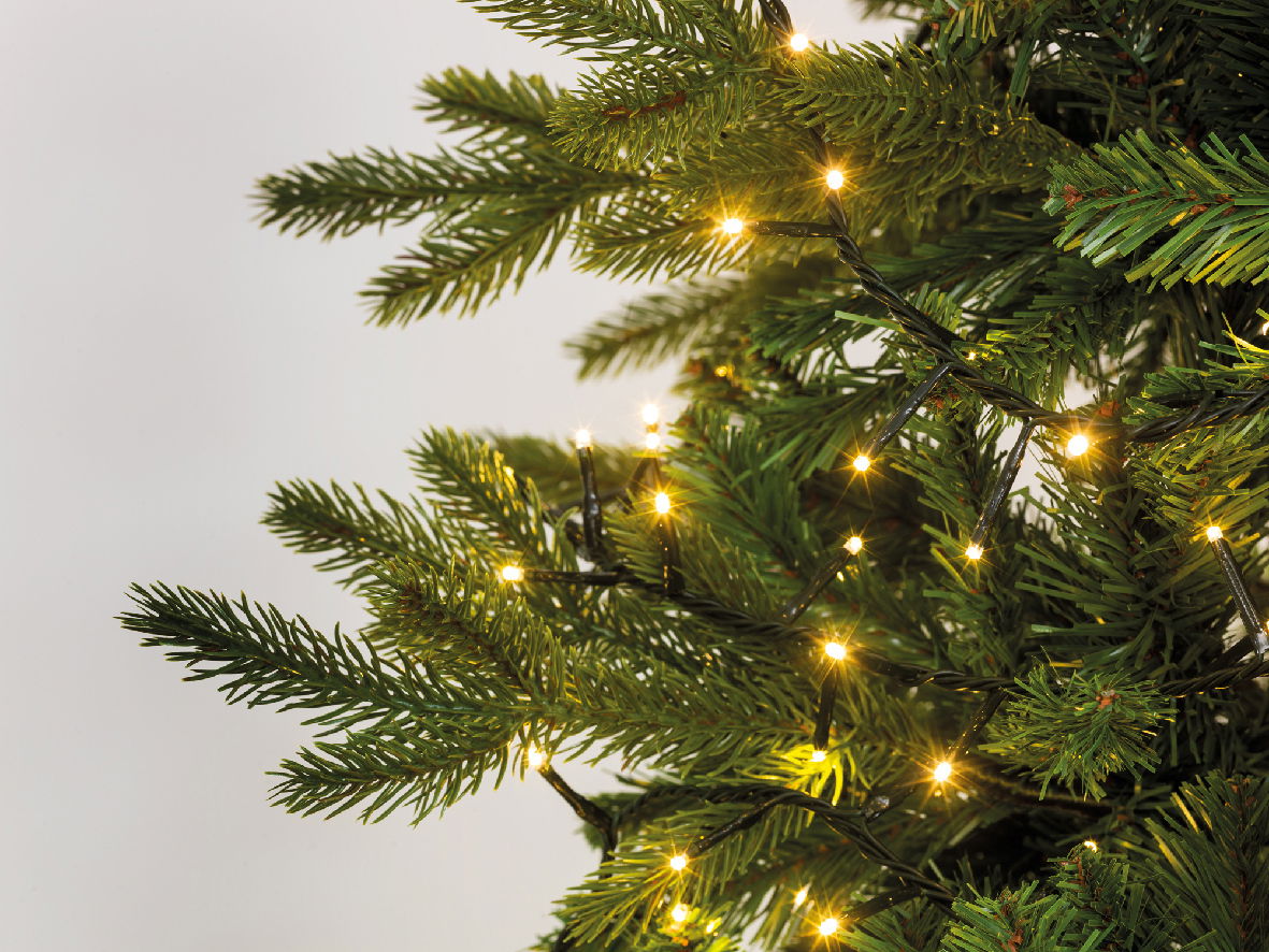 Nahaufnahme eines Weihnachtsbaums mit warmweißen LED-Lichtern, die in die Zweige eingewoben sind.