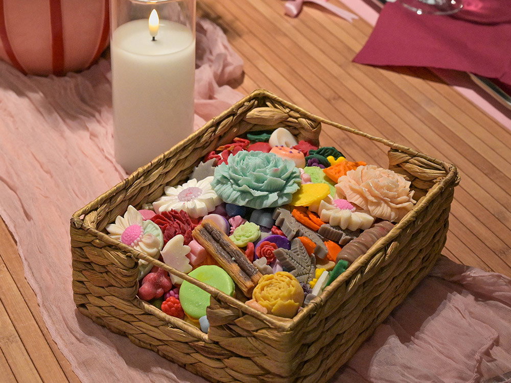Mand vol kleurrijke, gedetailleerde waselementen en bloemvormen tijdens een creatieve workshop kaarsen maken.