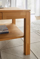 Nahaufnahme eines modernen Couchtisches aus Holz mit klaren Linien und einer unteren Ablage, auf der Bücher liegen. Der Tisch steht auf einem hellen Teppich in einem gut beleuchteten Raum.