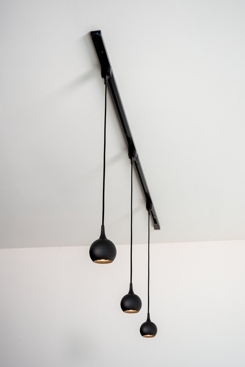 Zwarte hanglamp FAVORI met drie lampen, gefotografeerd van onderaf, met bolvormige lampenkappen die aan een rail hangen.