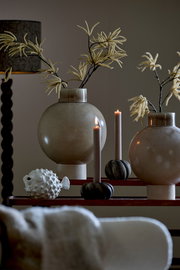 Dekorative Szene mit zwei großen, runden Vasen mit künstlichen Zweigen, zwei brennenden Kerzen in Haltern und einem weißen Fisch-Ornament. Die Perspektive ist frontal auf die Anordnung gerichtet.