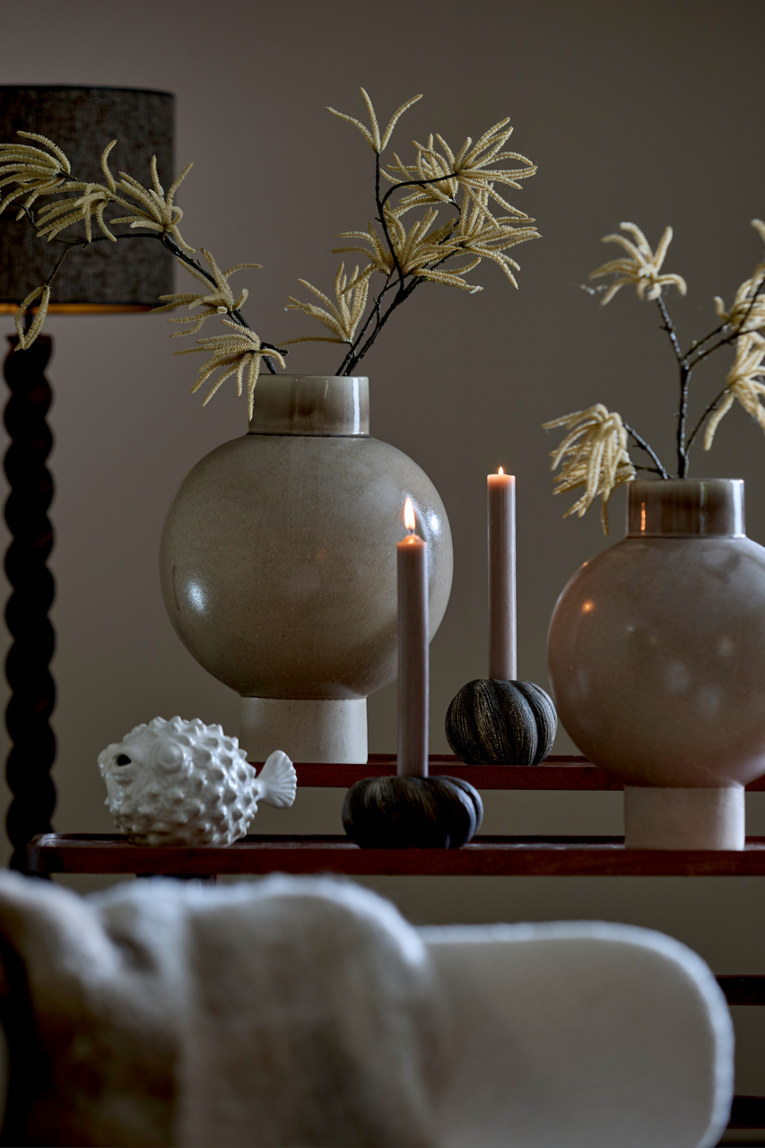 Dekorative Szene mit zwei großen, runden Vasen mit künstlichen Zweigen, zwei brennenden Kerzen in Haltern und einem weißen Fisch-Ornament. Die Perspektive ist frontal auf die Anordnung gerichtet.