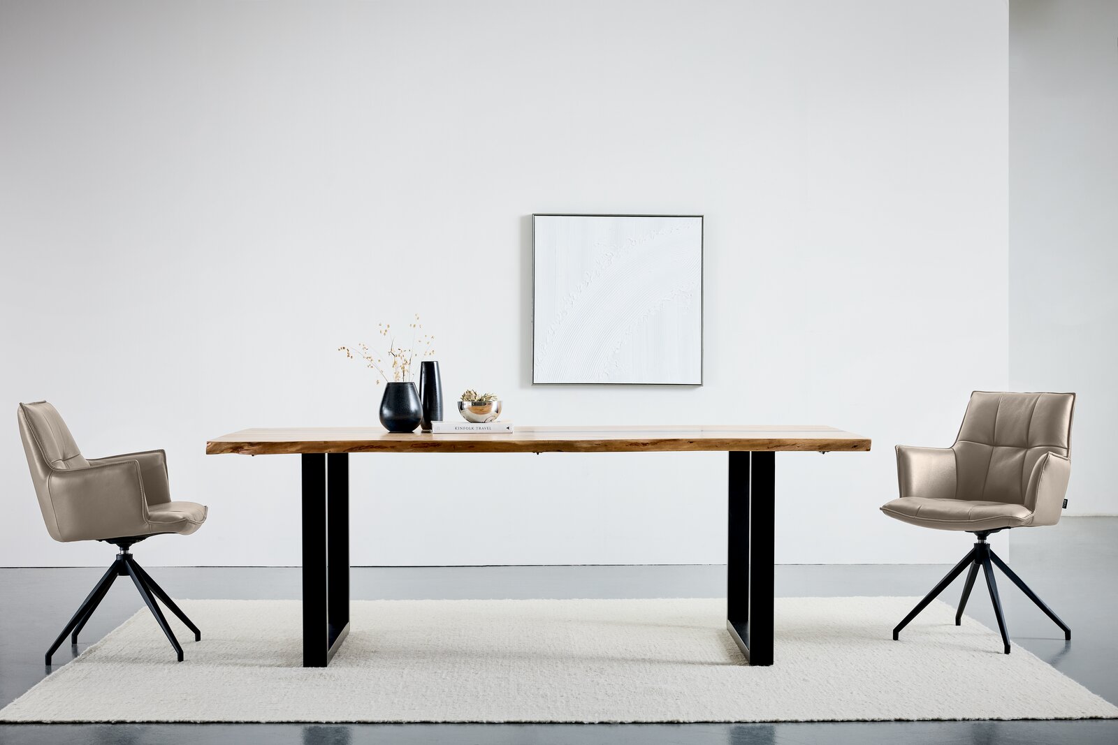 Moderner Esstisch mit massiver Holzplatte und schwarzen Metallbeinen, frontal in Augenhöhe fotografiert, zwischen zwei gepolsterten Drehstühlen in einem minimalistischen Raum.