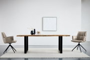 Moderne eettafel met een massief houten blad en zwarte metalen poten, van voren gefotografeerd op ooghoogte, tussen twee gestoffeerde draaistoelen in een minimalistische ruimte.