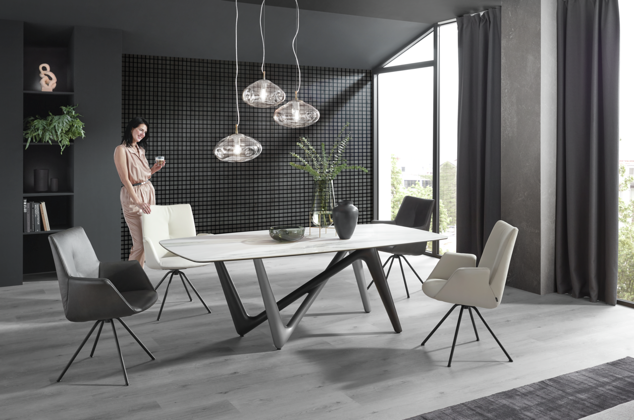 Moderner Esstisch mit einzigartigem, geometrischem Untergestell in einem stilvollen Esszimmer mit großen Fenstern und eleganten Stühlen, seitliche Perspektive.