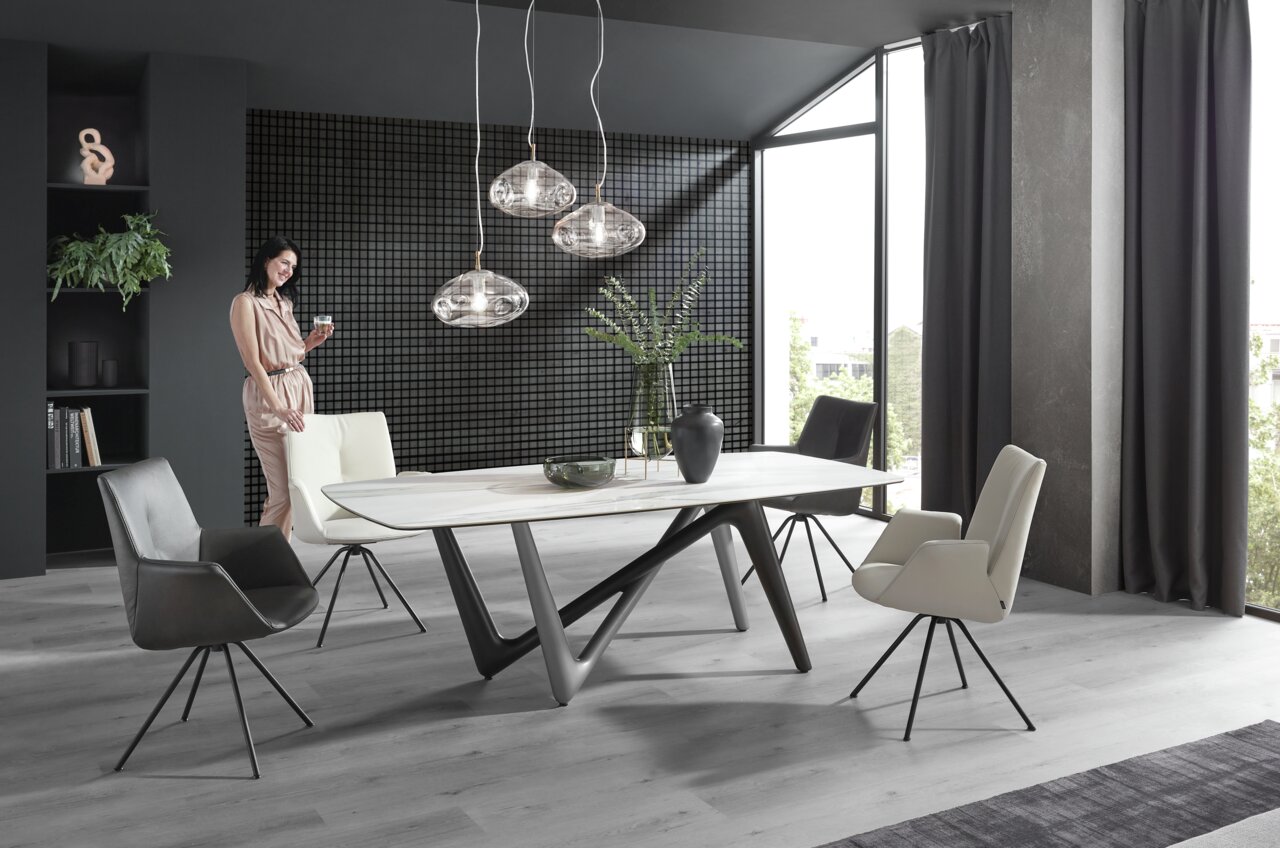 Moderner Esstisch mit einzigartigem, geometrischem Untergestell in einem stilvollen Esszimmer mit großen Fenstern und eleganten Stühlen, seitliche Perspektive.