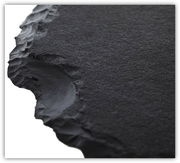 Nahaufnahme einer schwarzen, strukturierten Tischplatte mit unregelmäßigen Kanten, perspektivisch von der Seite aufgenommen.