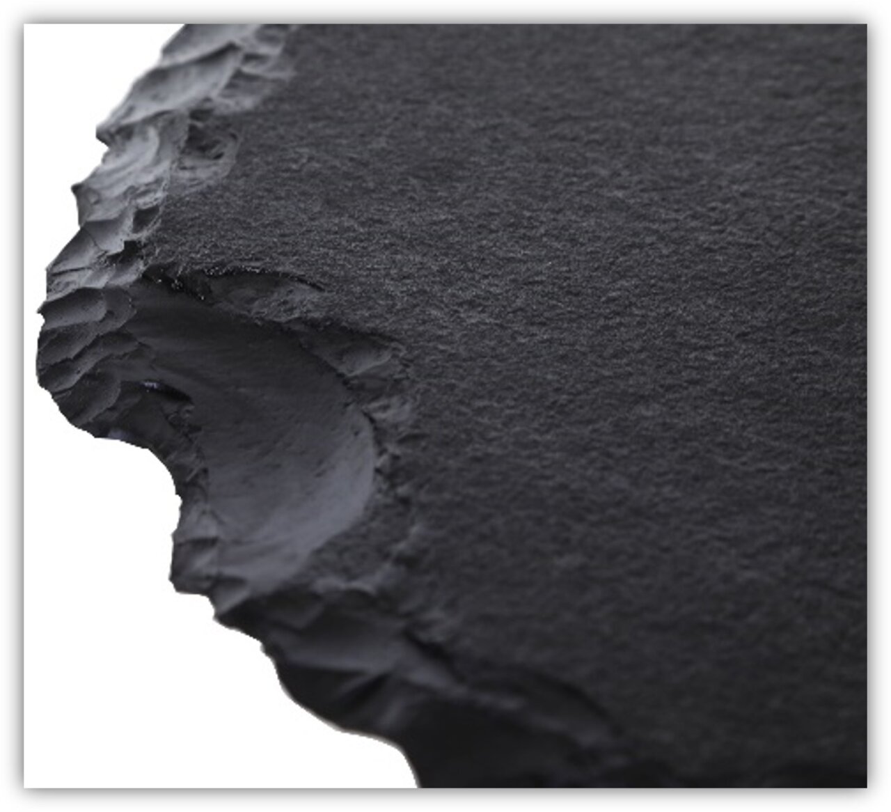 Nahaufnahme einer schwarzen, strukturierten Tischplatte mit unregelmäßigen Kanten, perspektivisch von der Seite aufgenommen.