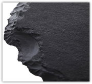 Nahaufnahme einer schwarzen, strukturierten Tischplatte mit unregelmäßigen Kanten, perspektivisch von der Seite aufgenommen.