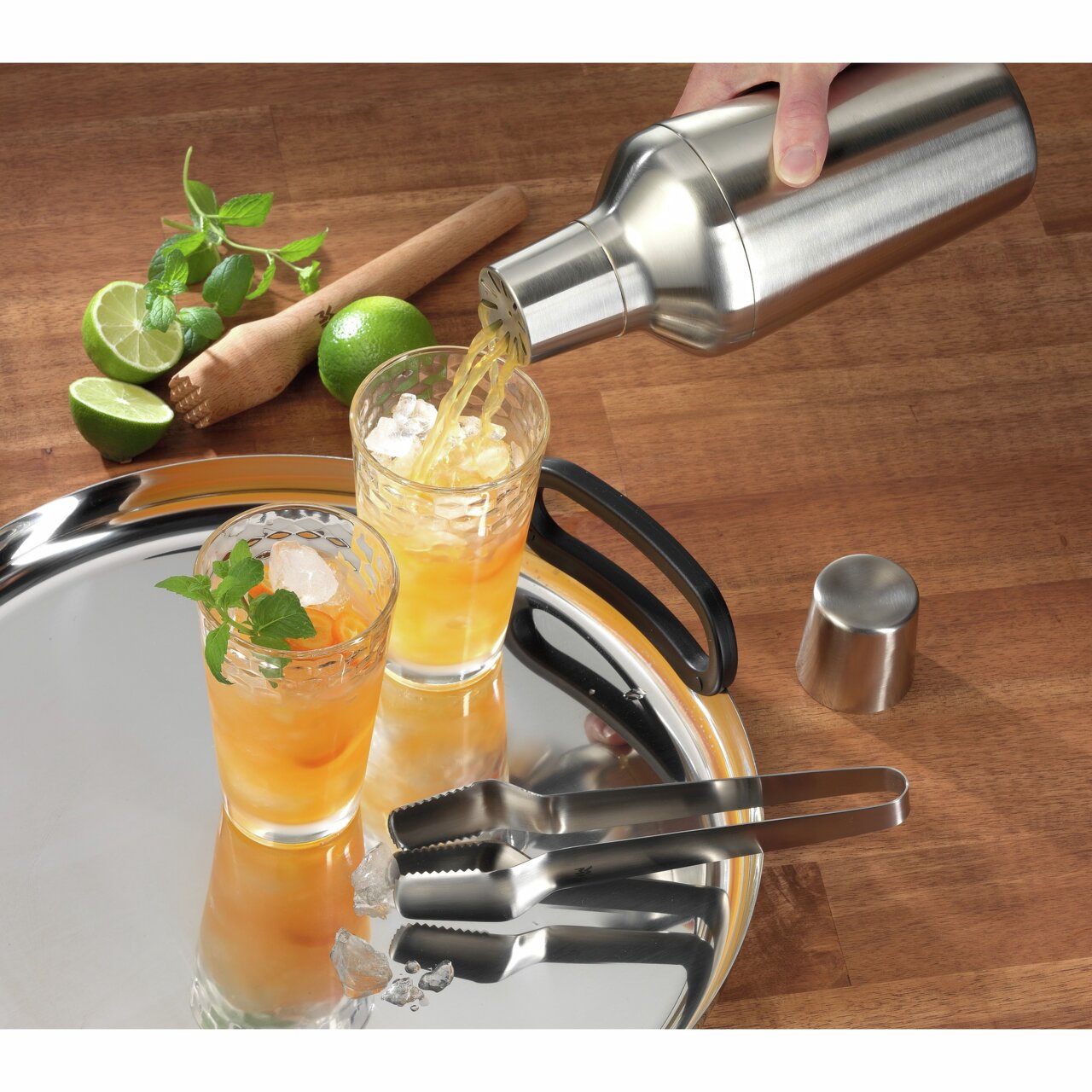Barset bestehend aus einem Sieb, Barmaß und Zange, mit einem Cocktailshaker, der aus der Vogelperspektive auf einem Tablett mit zwei Gläsern und frischen Zutaten gezeigt wird.