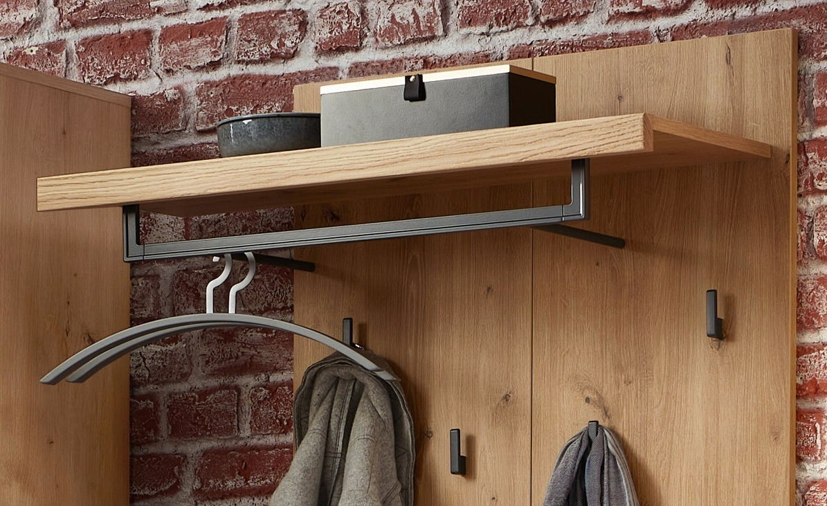 Nahaufnahme eines Garderobenpaneels aus Holz mit Ablage und Kleiderhaken, vor einer Ziegelwand montiert.