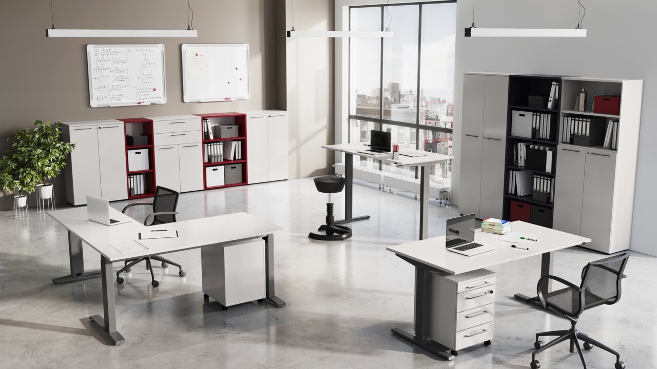 Moderne Büroumgebung mit mehreren Schreibtischen, Rollcontainern und Aktenschränken in einem hellen Raum mit großen Fenstern. Perspektive von schräg oben.