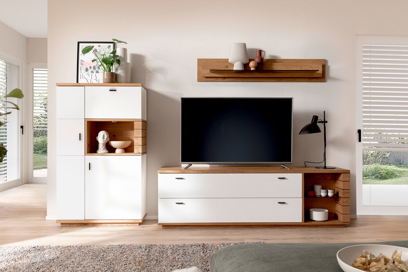 Moderne Wandkombination in einem Wohnzimmer mit weißem und holzfarbenem Design, bestehend aus einem hohen Schrank, einem TV-Schrank und einem Wandregal. Perspektive von vorne.