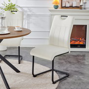 Cremeweißer Polster-Esszimmerstuhl mit Steppnähten und schwarzem Metall-Schwinggestell, seitliche Frontansicht im Wohn-/Essbereich neben rundem Holztisch und Kamin